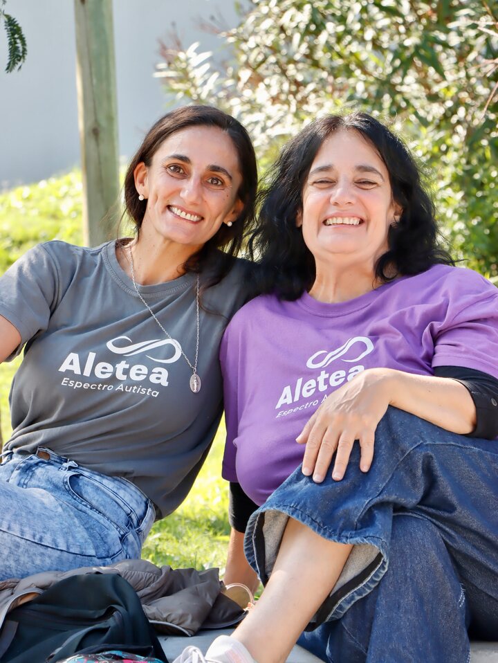 Dos personas sentadas al aire libre con camisetas de Aletea, en tonos gris y violeta.