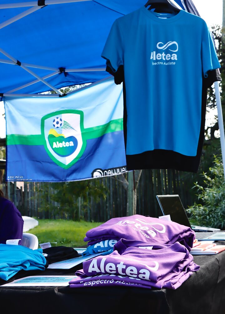 Camisetas de Aletea en una mesa y una camiseta azul colgada junto a una bandera del colectivo.
