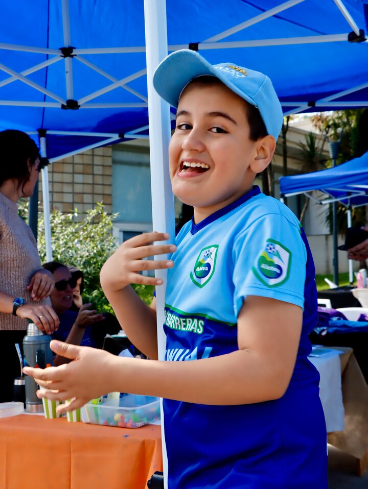 Una persona con gorra y camiseta azul junto a la mesa de Aletea, bajo el toldo.
