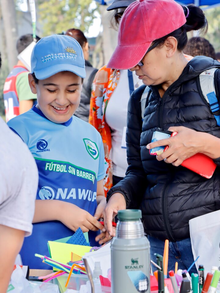Dos personas, una con gorra azul y otra con gorra roja, miran los materiales de una mesa.