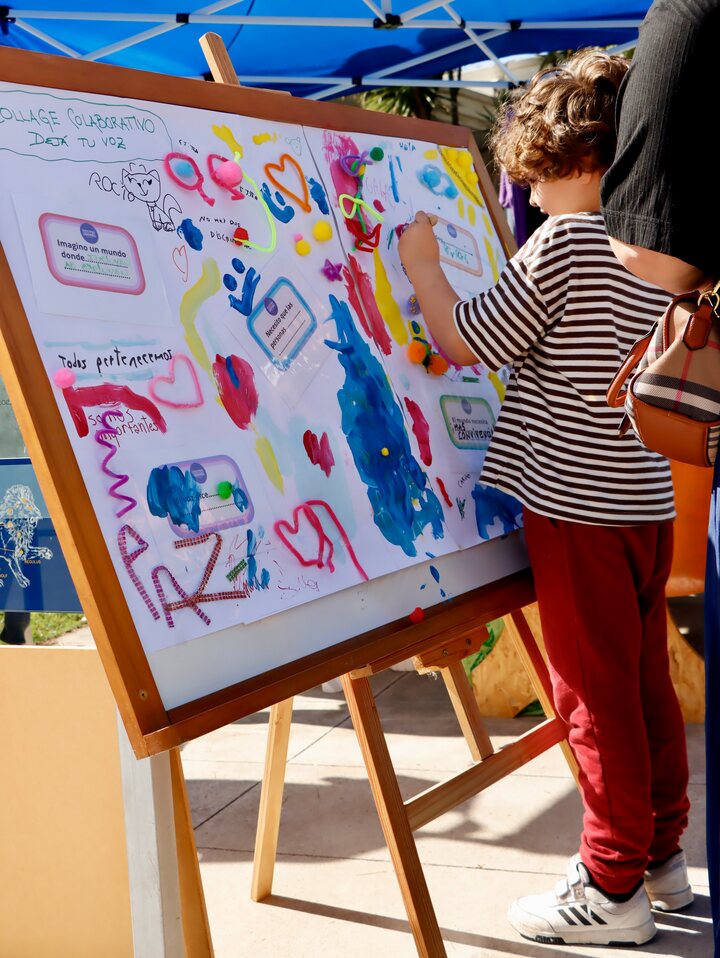 Una persona pinta un panel sobre un caballete; se ven colores, mensajes y el texto Collage colaborativo, Dejá tu voz.